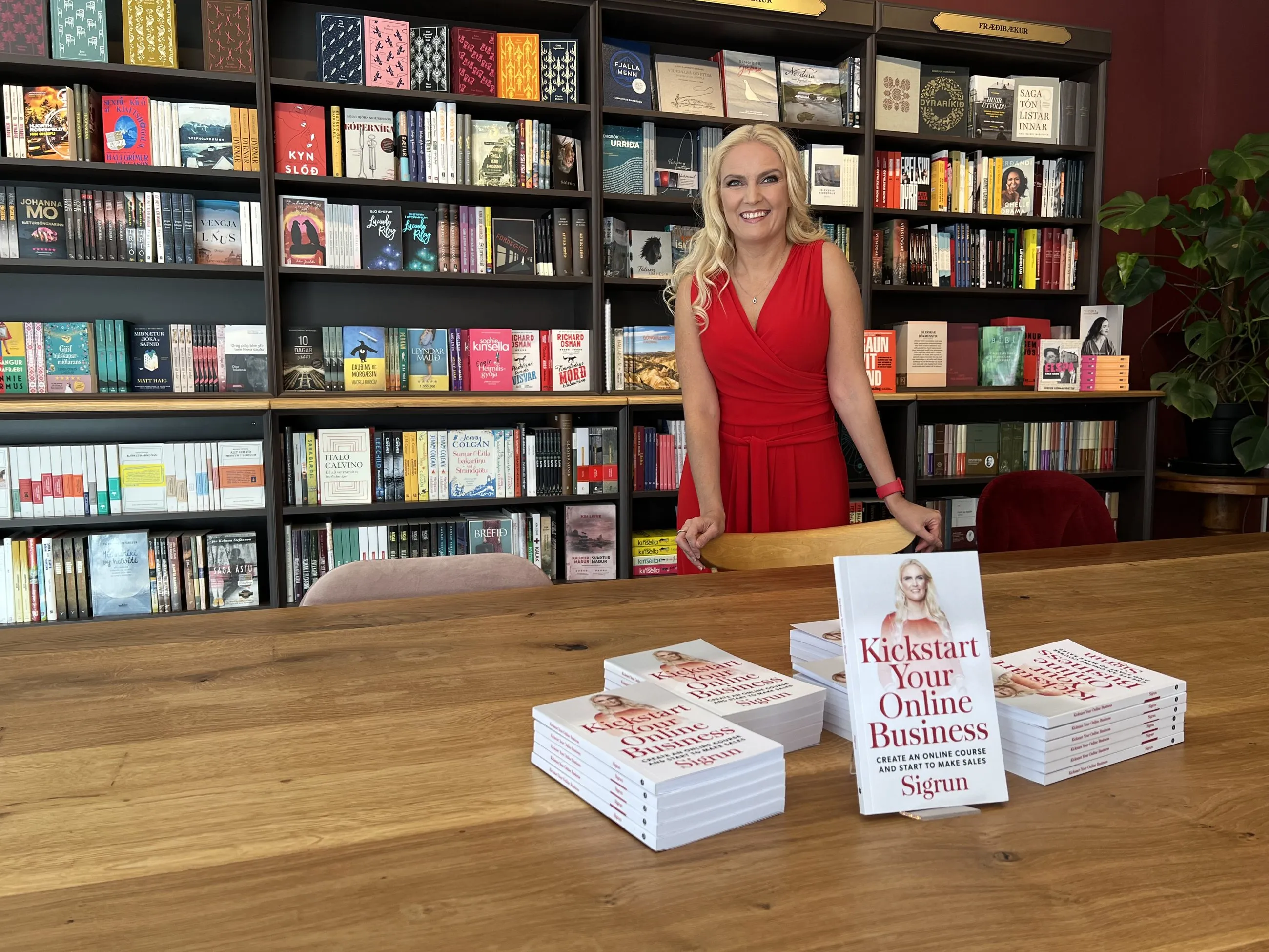 Sigrun in a red dress at her book launch in a bookshop, behind stacks of Kickstart Your Online Business