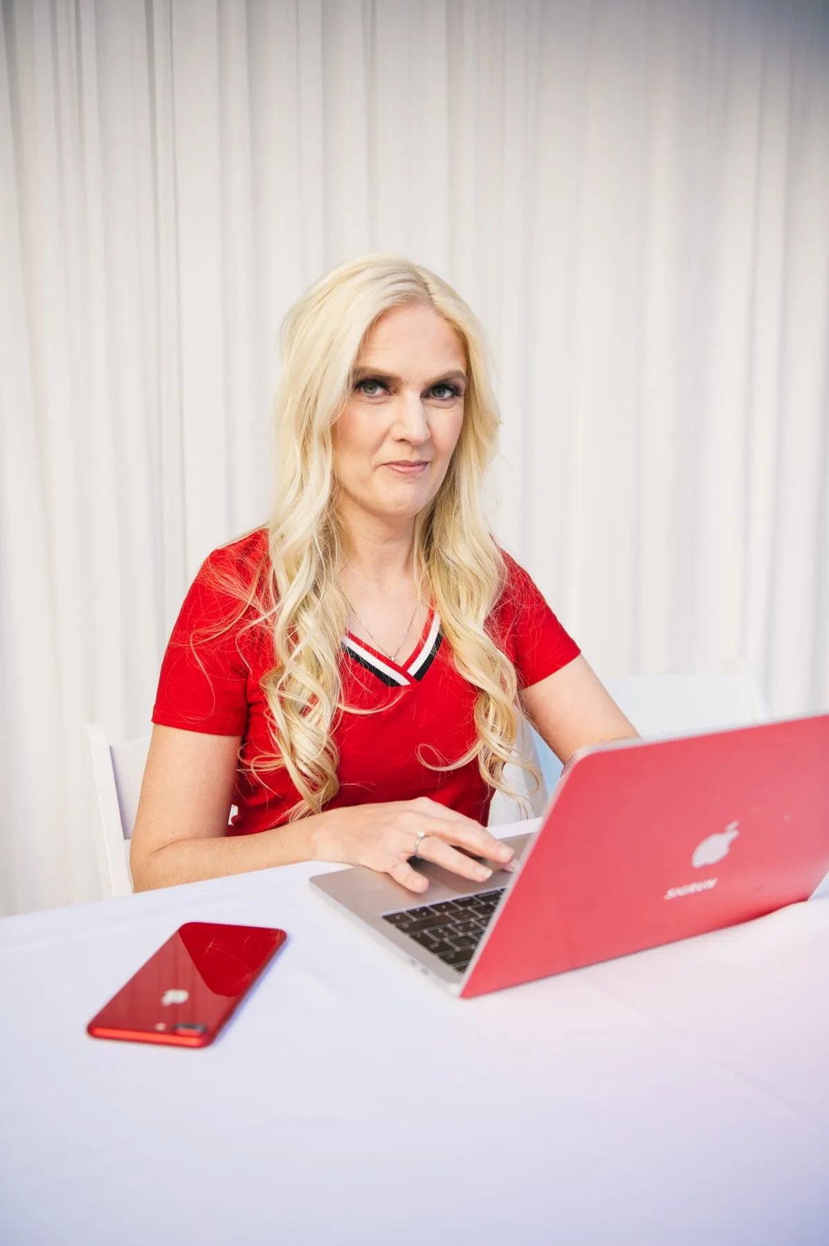 Sigrun in a red top working on her red laptop